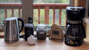 Eine Küchenarbeitsplatte mit Kaffeemaschine, Wasserkocher, Teekanne, einer Kaffeebohnenmischung in einem Glas und einem kleinen Behälter.