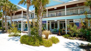 A beachfront hotel with multiple balconies, palm trees, and a sign for Olive Oil Outpost. - Amazing View, Updated Beachfront Condo (Bradenton Beach)