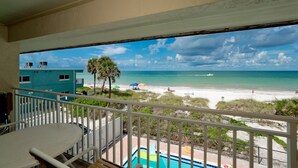 A balcony with a view of a beach, a pool, and a building with water tanks. - Amazing View, Updated Beachfront Condo (Bradenton Beach)