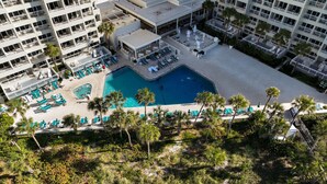 A rooftop pool area with lounge chairs and umbrellas, surrounded by palm trees and a multi-story building. - Updated Beachfront Condo at Prestigious Long Boat Key Resort (Longboat Key)