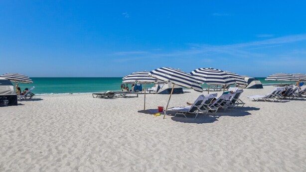 A beach with white sand, striped beach umbrellas, and lounge chairs. - Updated Beachfront Condo at Prestigious Long Boat Key Resort (Longboat Key)