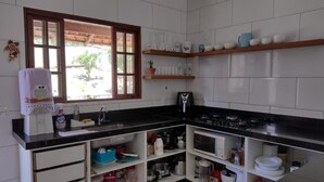 A compact kitchen with white cabinets, a black countertop, and a window with wooden frames. - Casa 3 Vale dos Reis Penedo com Piscina (Itatiaia)