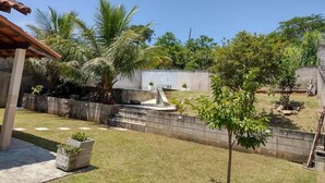 A backyard with a concrete patio, a small tree, and a stone wall. - Casa 3 Vale dos Reis Penedo com Piscina (Itatiaia)