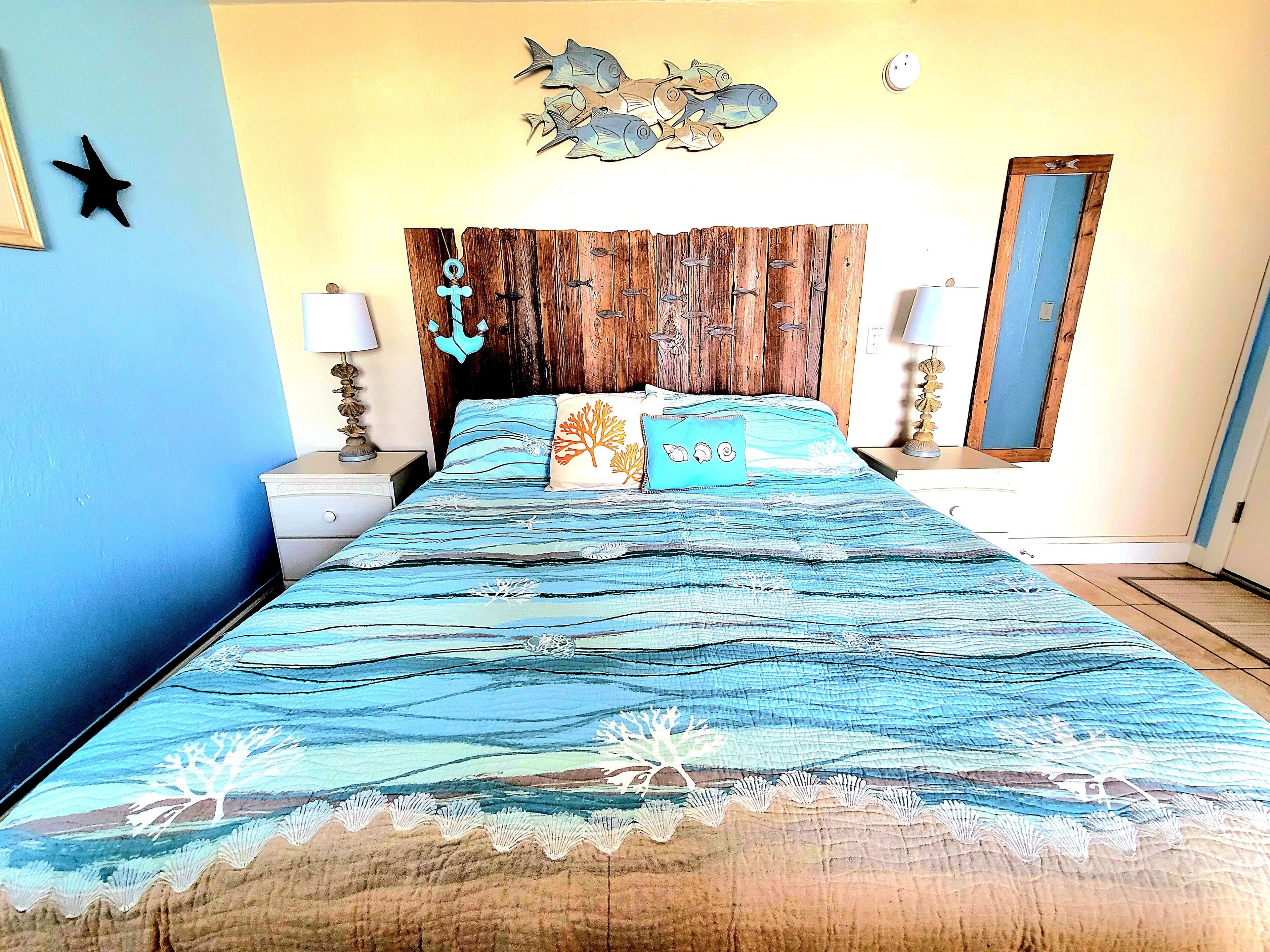 Un dormitorio con una cama, dos mesitas de noche, un cabecero de madera, una decoración de peces, una estrella y un espejo.