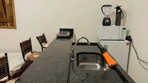 Et kompakt køkken med sort bordplade, vask, kaffemaskine, mikroovn og køleskab.