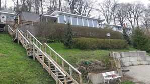Uma área residencial com uma escadaria de madeira que leva a uma casa, um muro de pedra e um banco.