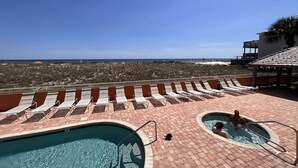 Zona de piscina con sillones reclinables y un jacuzzi, con vista a una playa y cielo despejado.