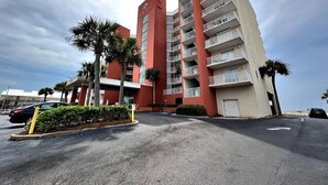 Un hotel de varios pisos con fachada roja y color crema, balcones y palmeras al frente.
