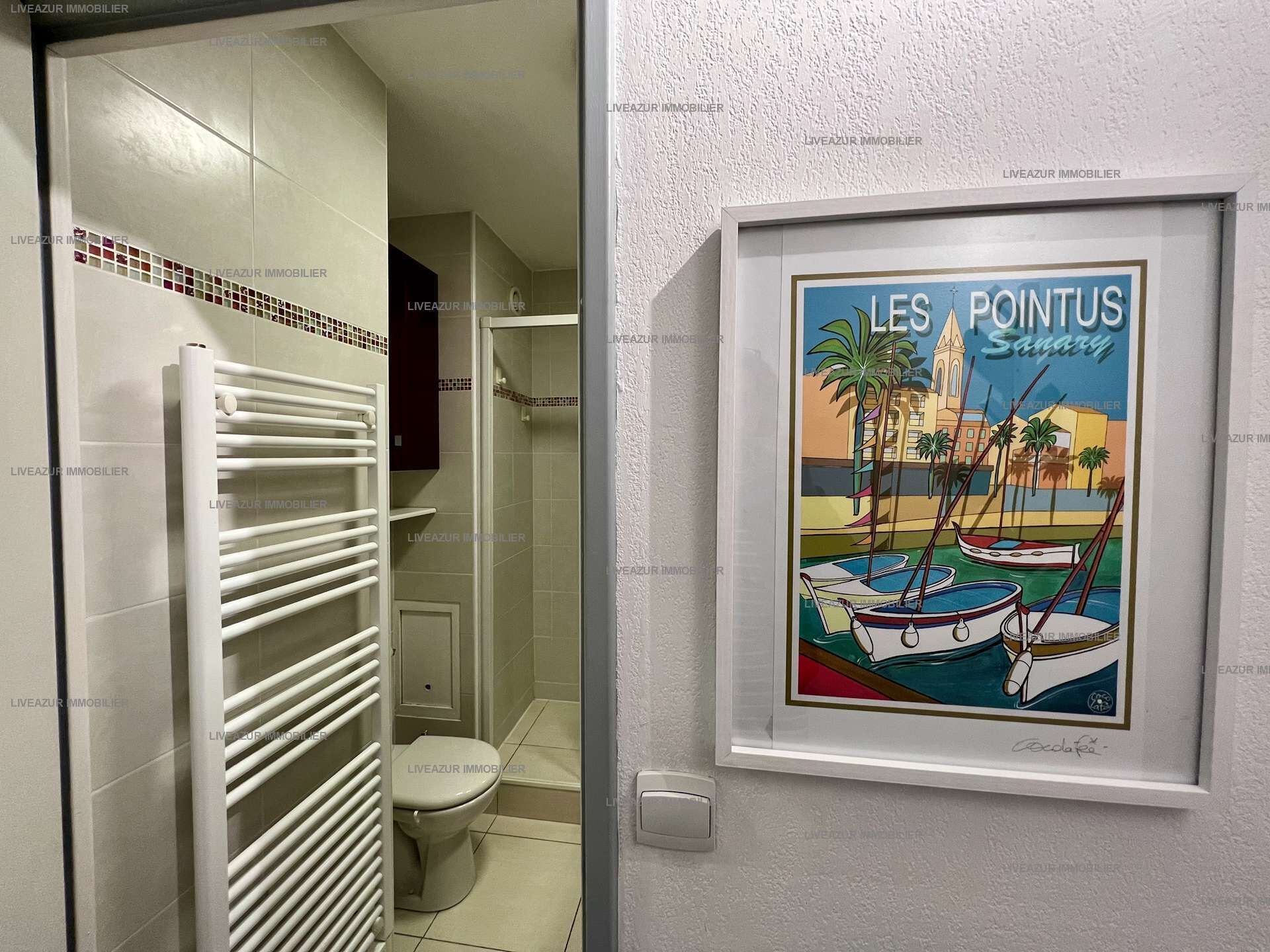 Une salle de bain avec un radiateur blanc, des toilettes et une affiche encadrée représentant « Les Pointus Sanary ».