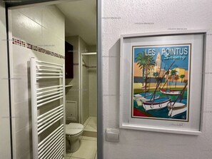 A bathroom with a white radiator, a toilet, and a framed poster of 'Les Pointus Sanary'. - Renovated studio in residence with swimming pool for 4 (SANARY SUR MER)