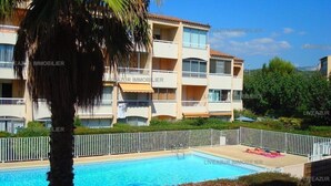 Un hôtel doté d’une piscine, entouré d’une clôture blanche, avec un palmier au premier plan.