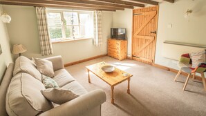 A cozy living room with a sofa, a wooden coffee table, a television on a wooden cabinet, and a chair with colorful cushions. - Lower House B&B (Craven Arms)