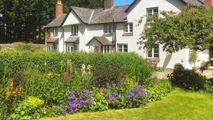 A two-story house with a white exterior and a garden in front. - Lower House B&B (Craven Arms)