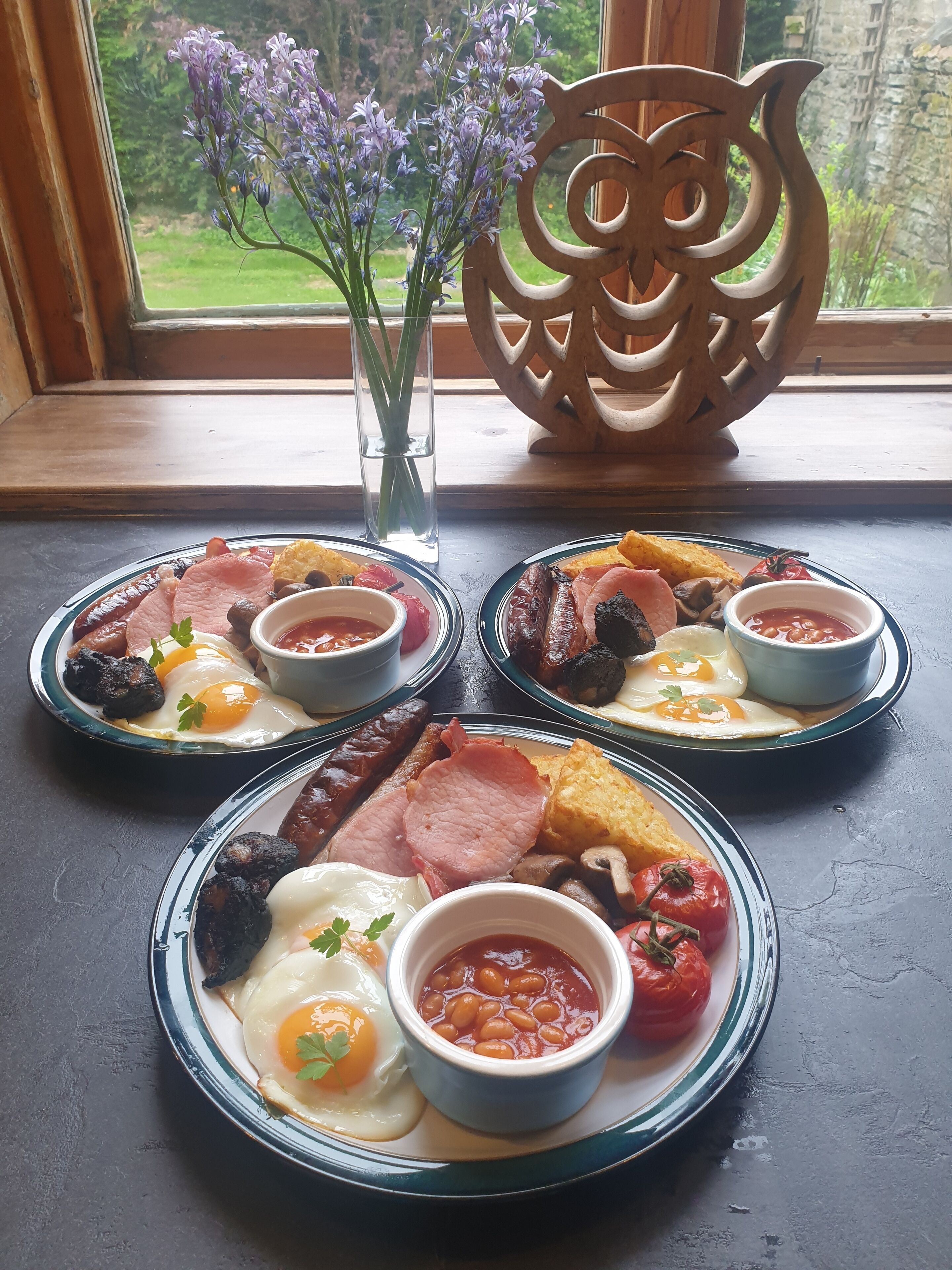 Three plates of breakfast food on a table by a window with a view of greenery.