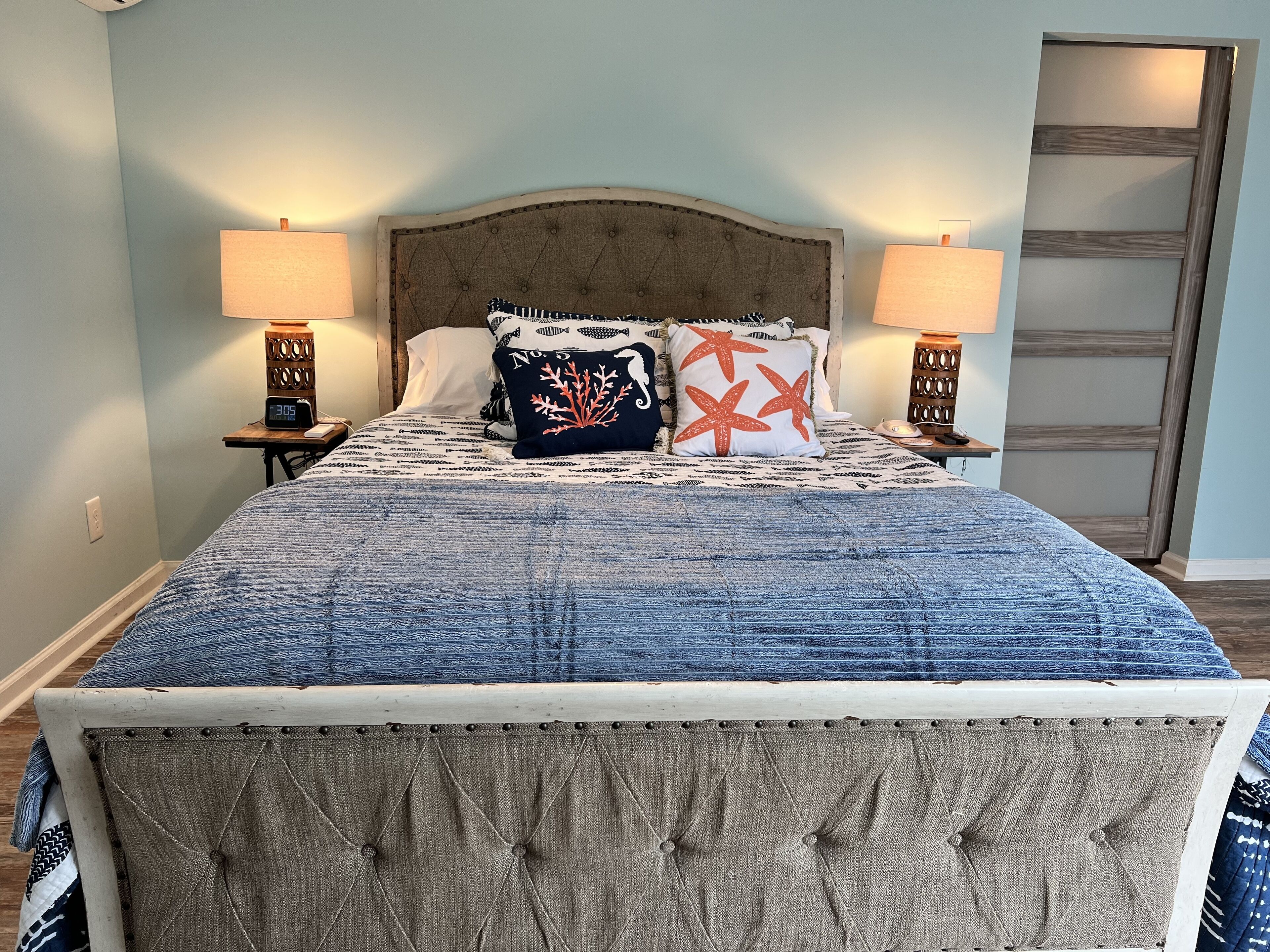 Een slaapkamer met een gebutst hoofdeinde, een bed met een decoratieve spreideken en twee bedlampjes.