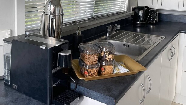 Eine moderne Küche mit integrierter Kaffeemaschine, Wasserkocher und Spüle. Auf der Arbeitsfläche stehen Gläser mit Snacks.