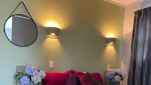 Ein Zimmer mit einem Bett, einem Sessel, zwei Wandleuchten, einem Spiegel und zwei Blumenarrangements.