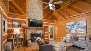 A log cabin interior with a stone fireplace, a television mounted above it, a sofa, and a coffee table. - Private, Peaceful Log Cabin w/ wrap around porch and fireplace. Central location (Boone)
