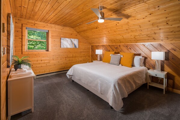 A wooden-paneled bedroom with a bed, bedside lamps, a nightstand, a window, and a ceiling fan. - Private, Peaceful Log Cabin w/ wrap around porch and fireplace. Central location (Boone)
