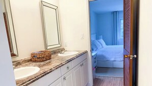 A bathroom with a sink, mirror, and a wicker basket on the countertop. - Sea Shell Room — Bright Coastal Luxury with Extra Space to Unwind (Rehoboth Beach)