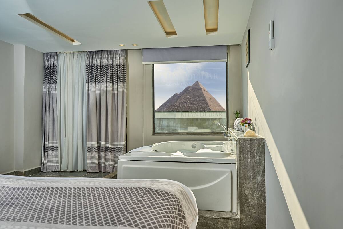 A modern bathroom with a large bathtub, a view of a pyramid, and a window with curtains.