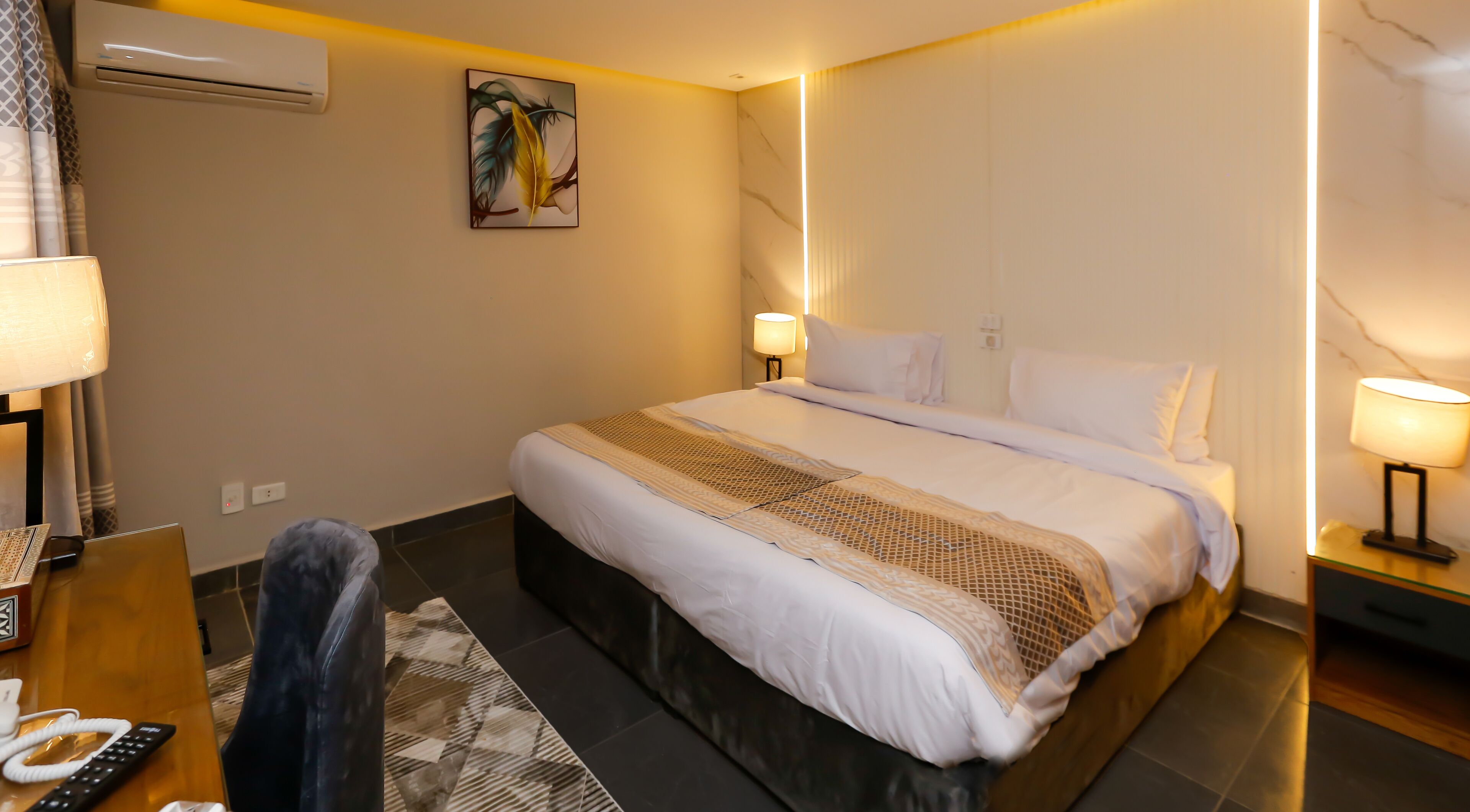 A hotel room with a large bed, bedside lamps, a desk with a telephone, and a painting on the wall.