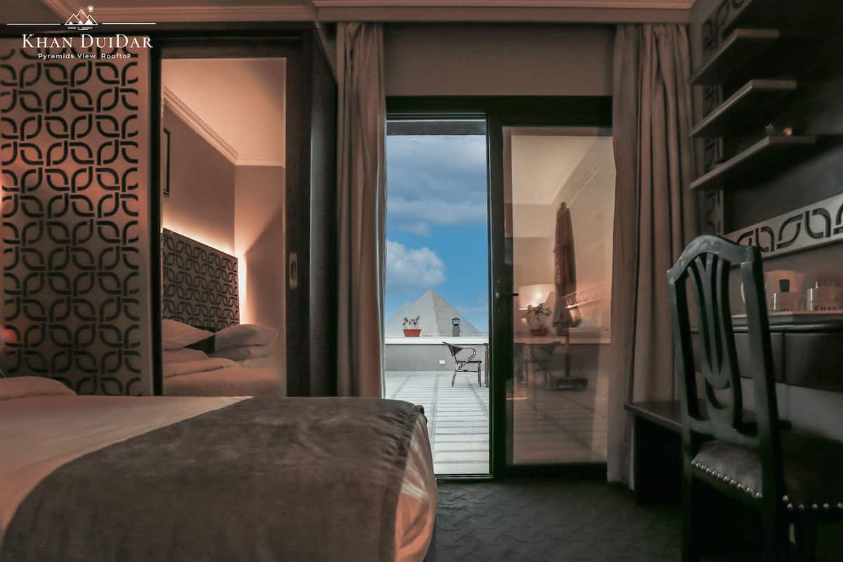 A hotel room with a bed, a desk, and a view of a pyramid.