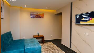 Una sala moderna con un sofá azul, una mesita de madera con una planta, un cuadro en la pared y un televisor mostrando un anuncio de Viernes Negro.