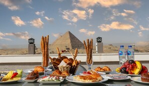 A table set with various foods and drinks, a pyramid in the background, and a clear sky.