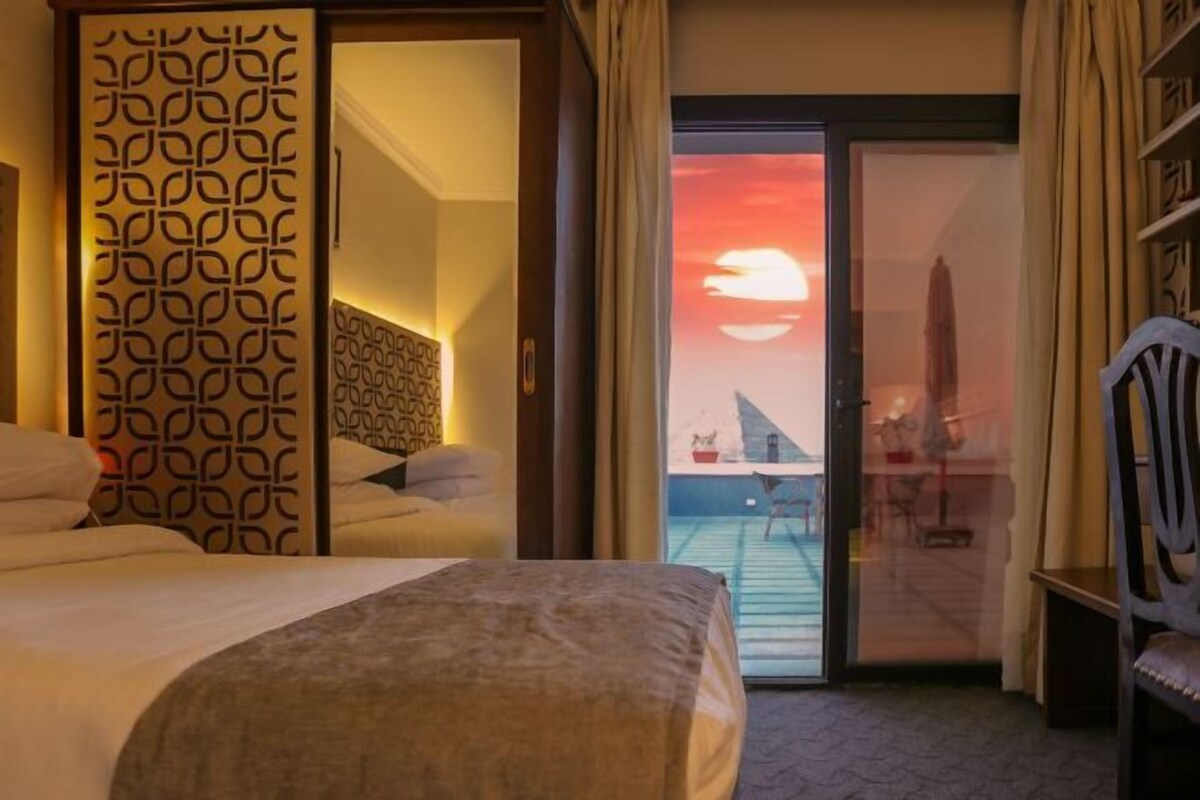 Habitación de hotel con cama, separador decorado y vista al atardecer a través de un ventanal.