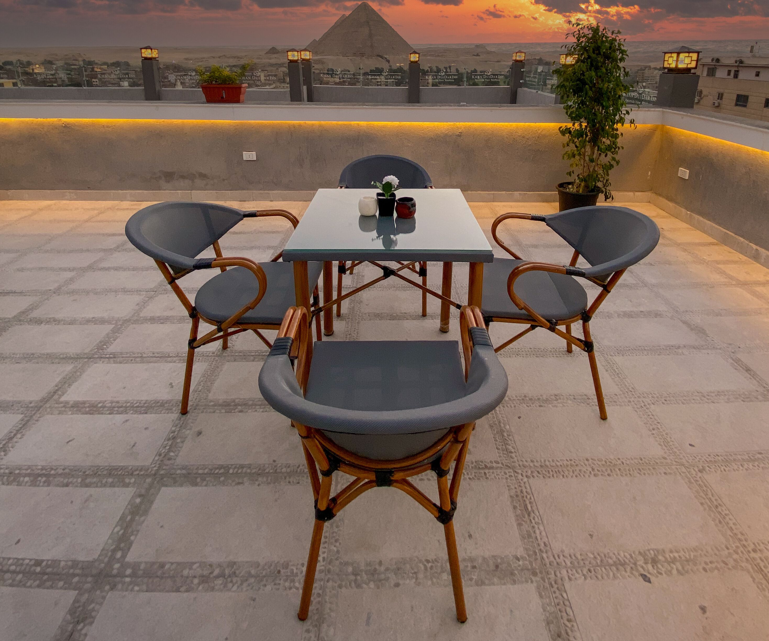 A rooftop terrace with a table and chairs, a potted plant, and a view of the pyramids.