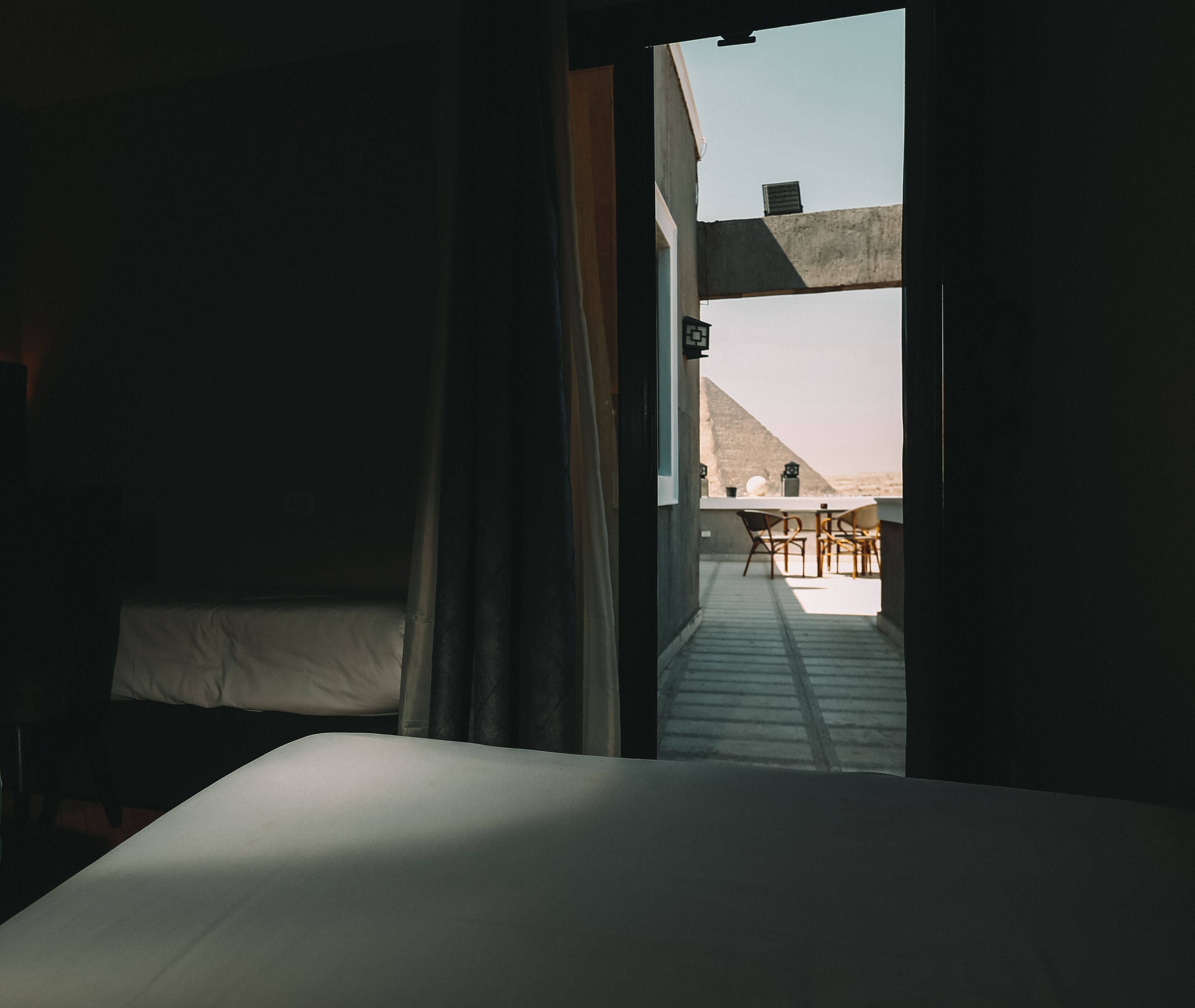 A bedroom with a bed, a window, and a view of an outdoor terrace with a table and chairs.