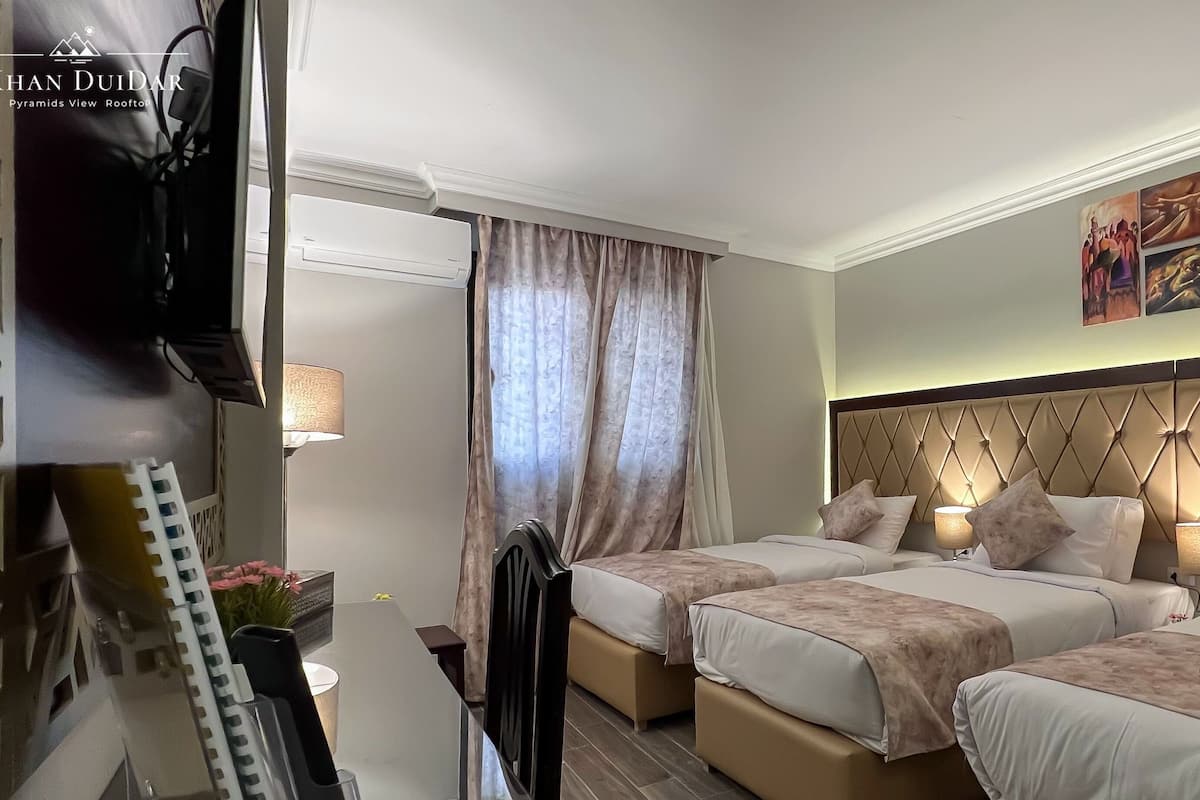 A hotel room with two beds, a TV, a desk, and a window with curtains.