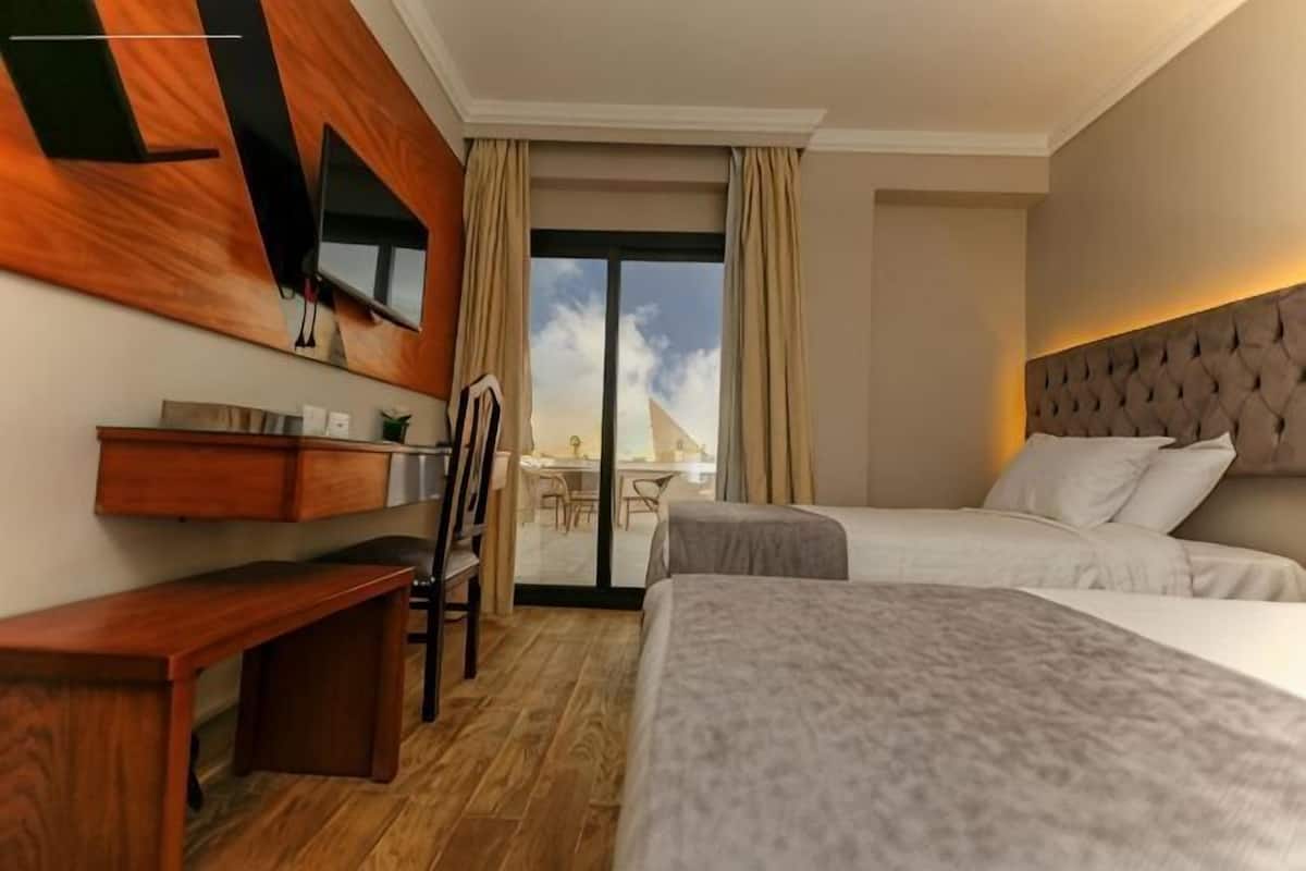 A hotel room with a bed, a desk, a chair, a TV, and a balcony with a view.