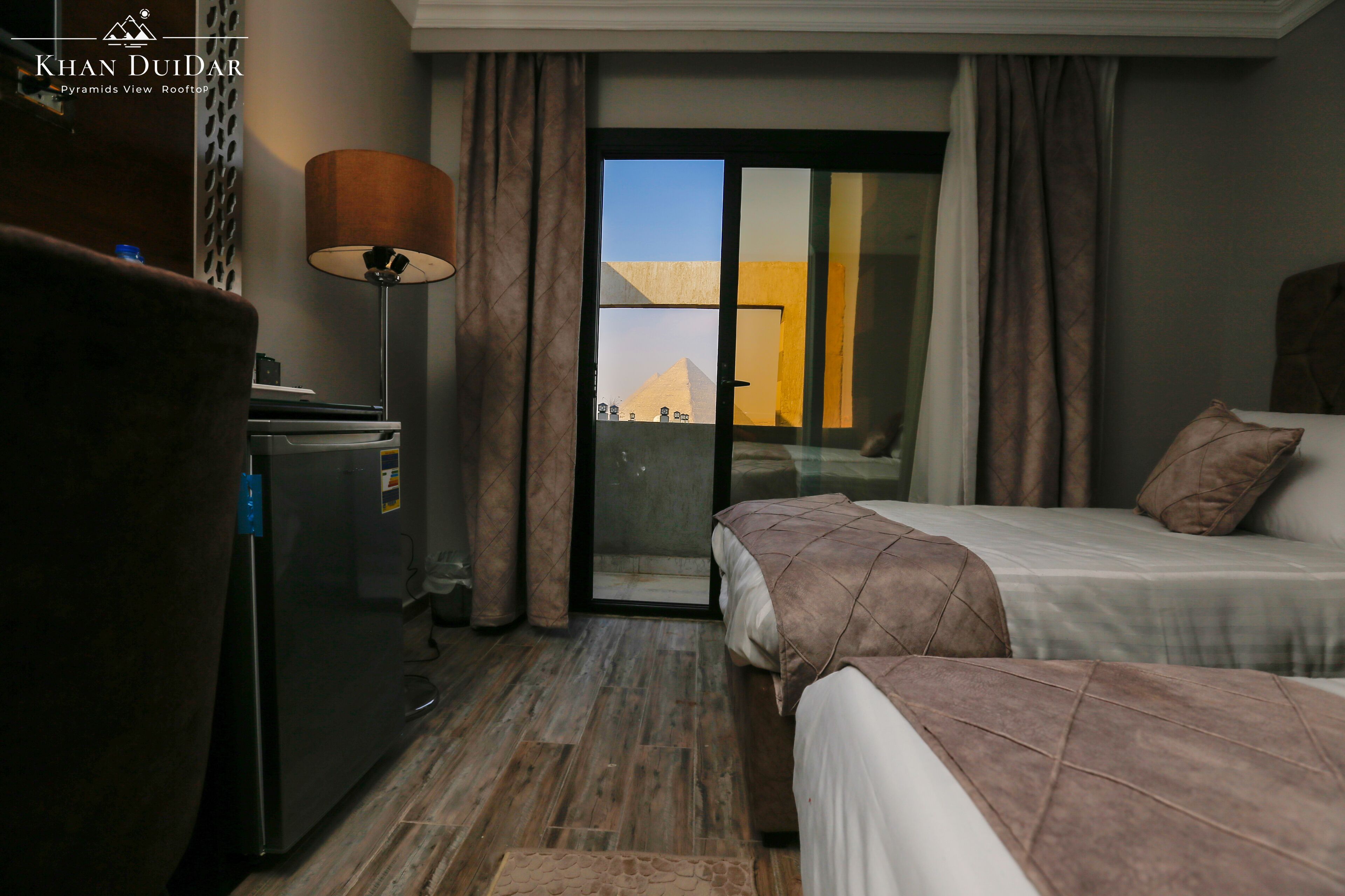 A hotel room with a bed, a desk, a lamp, and a view of pyramids.