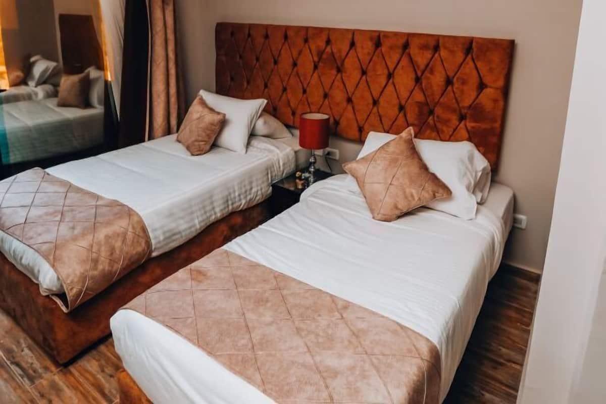 Two adjacent beds with headboards, a bedside table with a lamp, and a mirror on the wall.