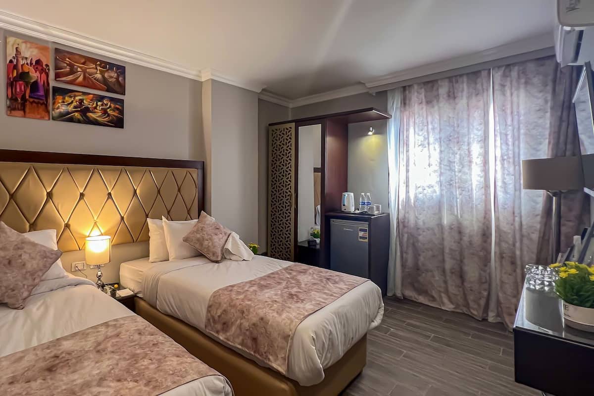 A hotel room with two beds, a decorative headboard, a minibar, and a view of the outdoors.