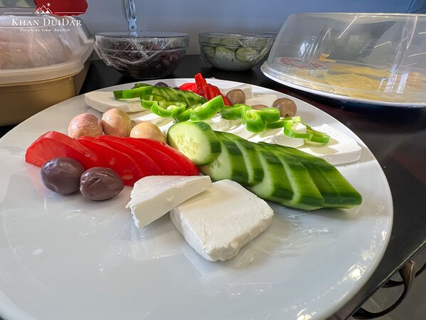 A plate of assorted cheeses, olives, and sliced vegetables.