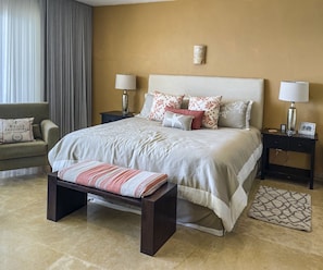A neatly arranged bedroom with a large bed, two bedside tables, a bench, and a patterned rug. - Luxury Beach Front Condo in Beautiful Punta de Mita (Punta de Mita)