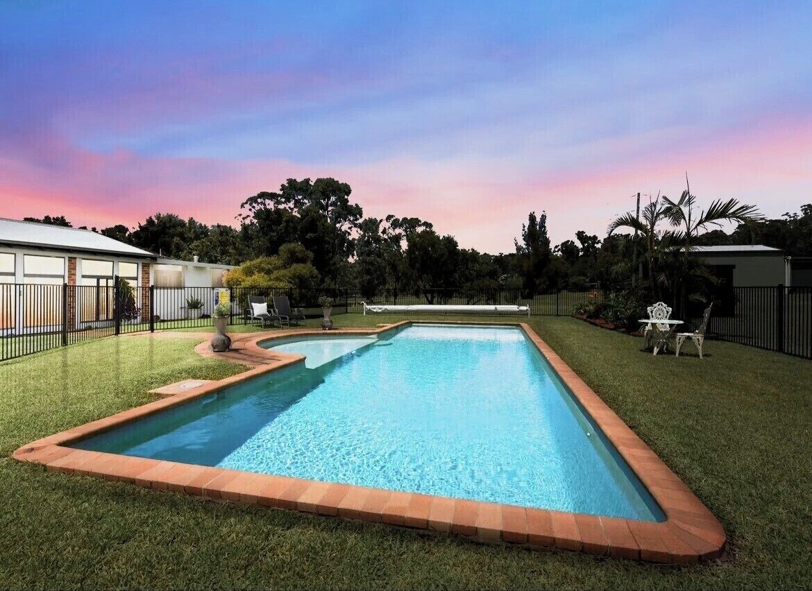 A rectangular swimming pool with a brick border, surrounded by well-maintained grass and trees.