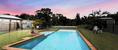 A rectangular swimming pool with a brick border, surrounded by well-maintained grass and trees.