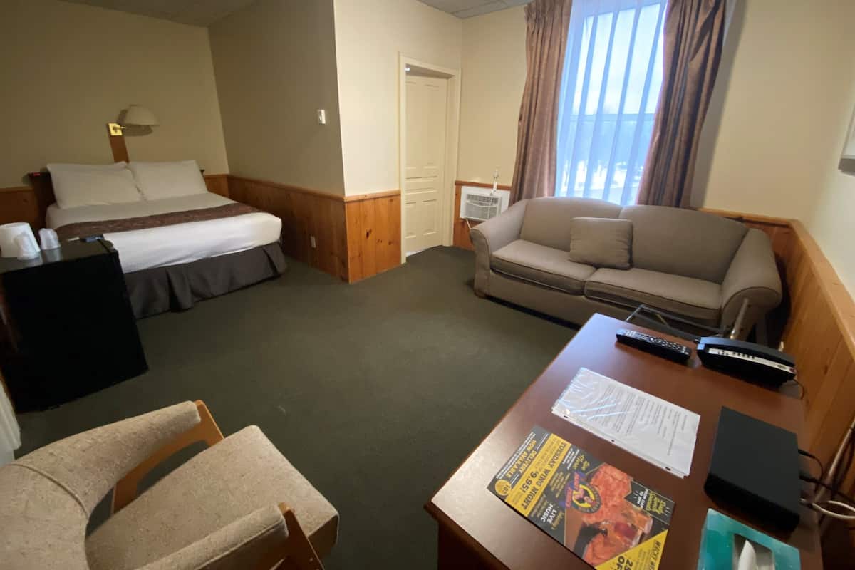 A hotel room with a bed, a sofa, a desk with a remote control, and a window with curtains.