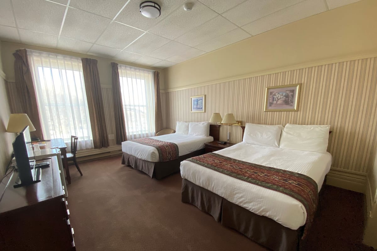 A hotel room with two beds, a desk, a chair, and a window with curtains.