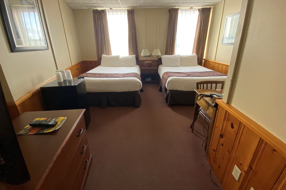 A hotel room with two beds, a desk with a computer, and a chair.