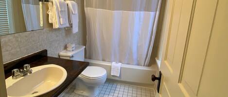 A bathroom with a white sink, toilet, and bathtub. There is a shower curtain and a towel rack with towels.