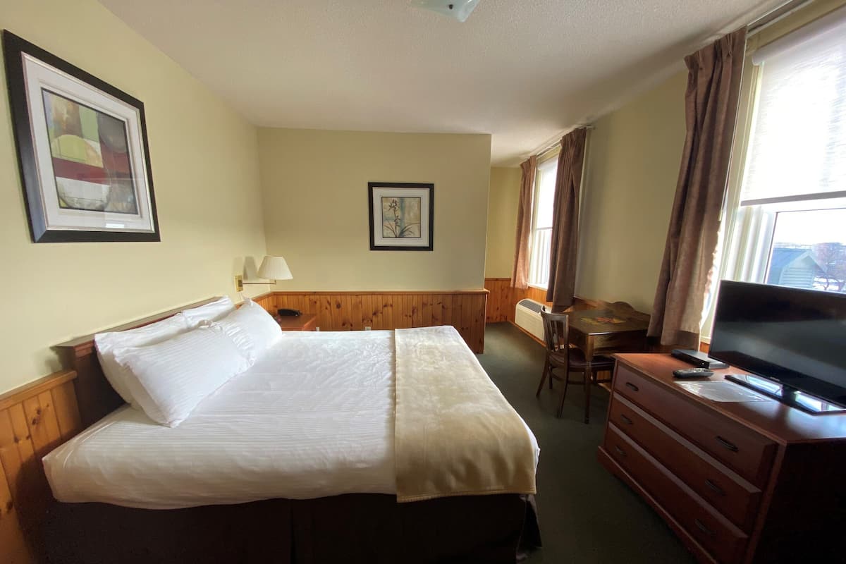 A hotel room with a large bed, a desk, a chair, a television, and a window with curtains.