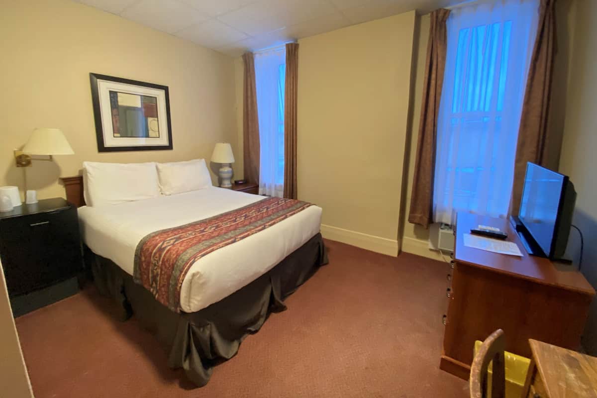 A hotel room with a bed, bedside tables, a desk with a computer, and a television.