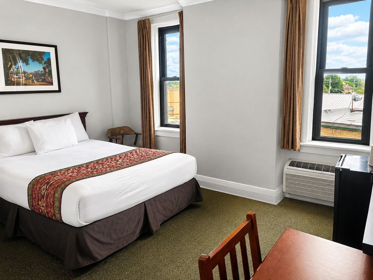 Une chambre d’hôtel avec un lit, une chaise, un bureau, un radiateur et une fenêtre avec des rideaux.