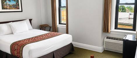 Quarto de hotel com cama, cadeira, escrivaninha, aquecedor e janela com cortinas.