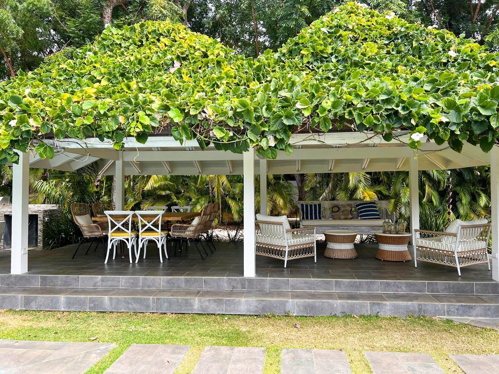 A covered outdoor seating area with wicker furniture and a pergola with climbing plants.